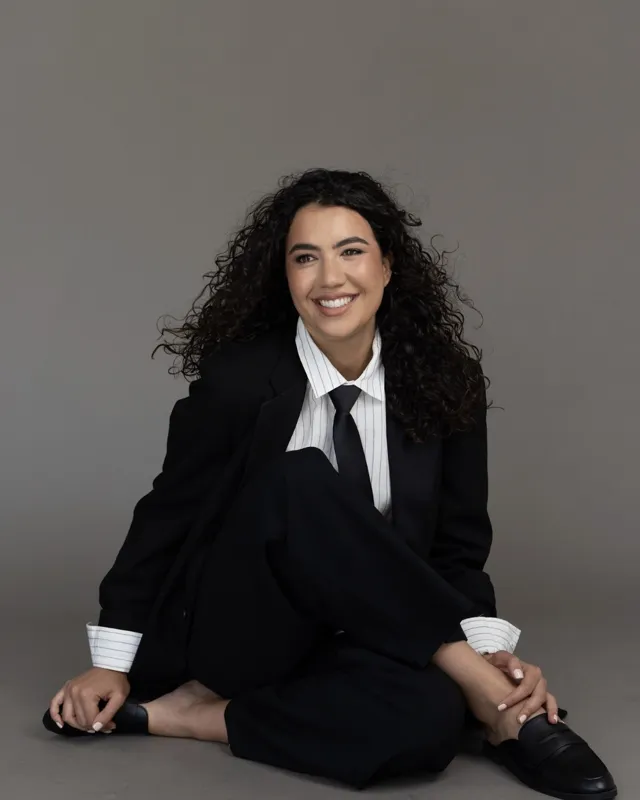 Aurora in a black suit, sitting on the floor, smiling